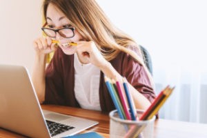 Woman biting her pencils looking at her laptop