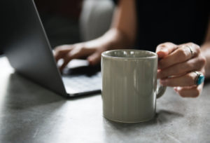 woman holding a cup of coffee next to laptop