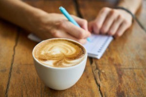 cup of coffee and person writing in a notebook