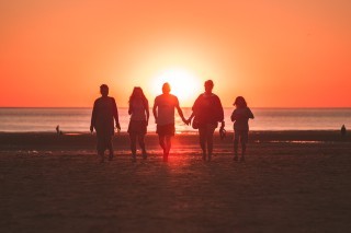group holding hands walking in front of sunset in ocean