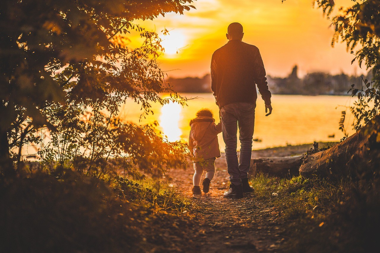 A father and daughter walking toward water at sunset