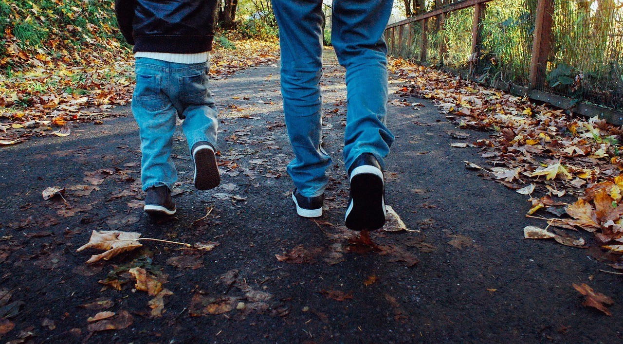 a parent and son walking on a path with leaves